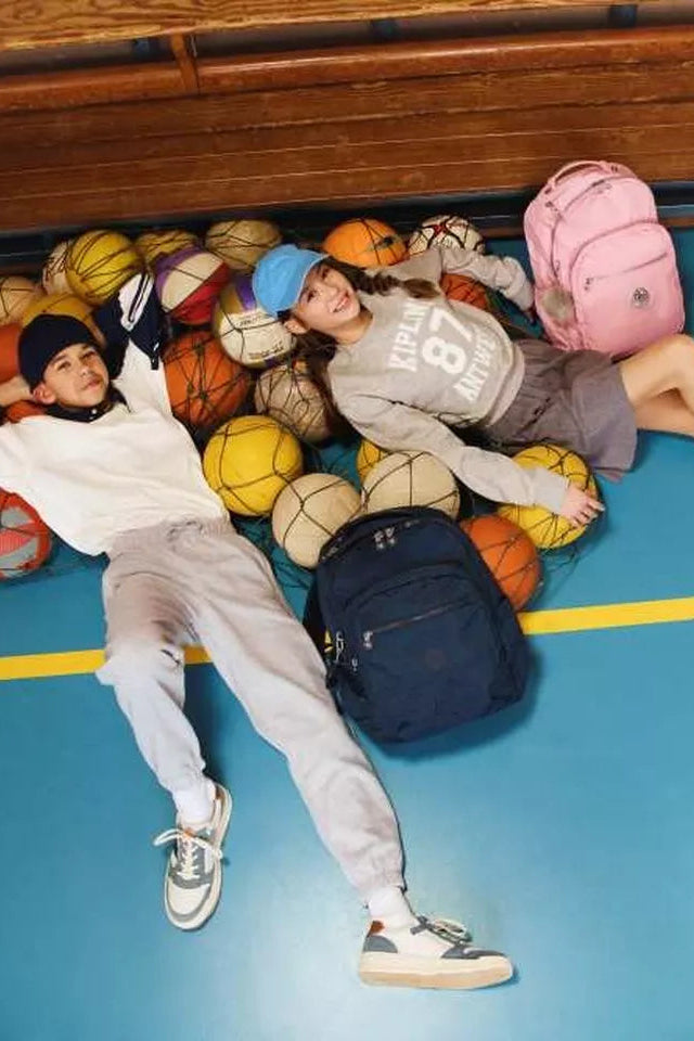 Two people lying on a blue floor with colorful balls and backpacks