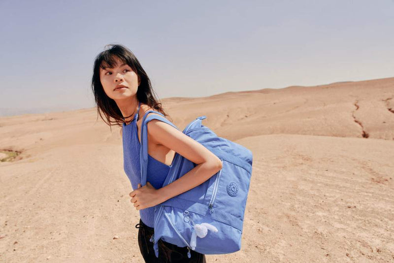 Person wearing a blue top and carrying a matching Kipling blue bag in a desert setting