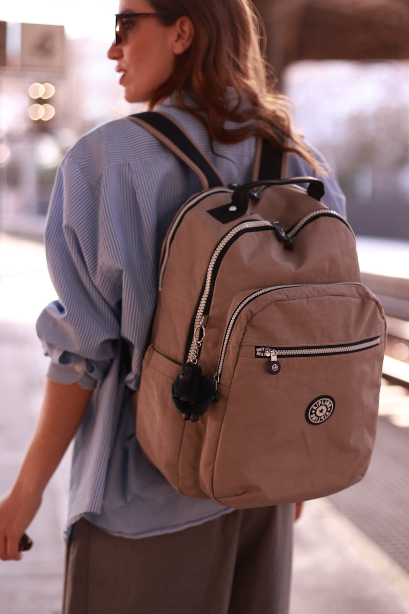 Person wearing a brown backpack with a visible brand logo.