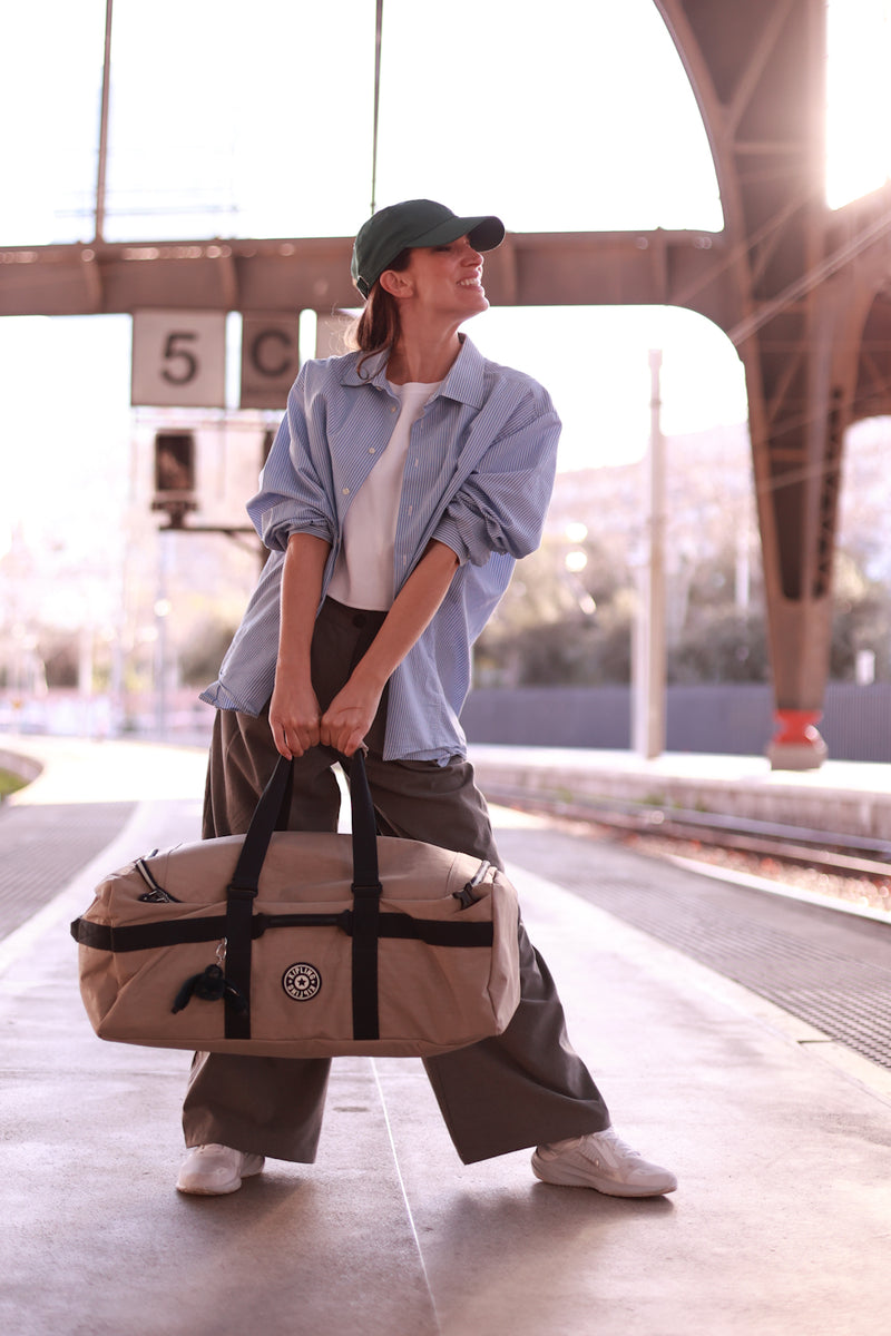 Person holding a beige travel bag at a train station